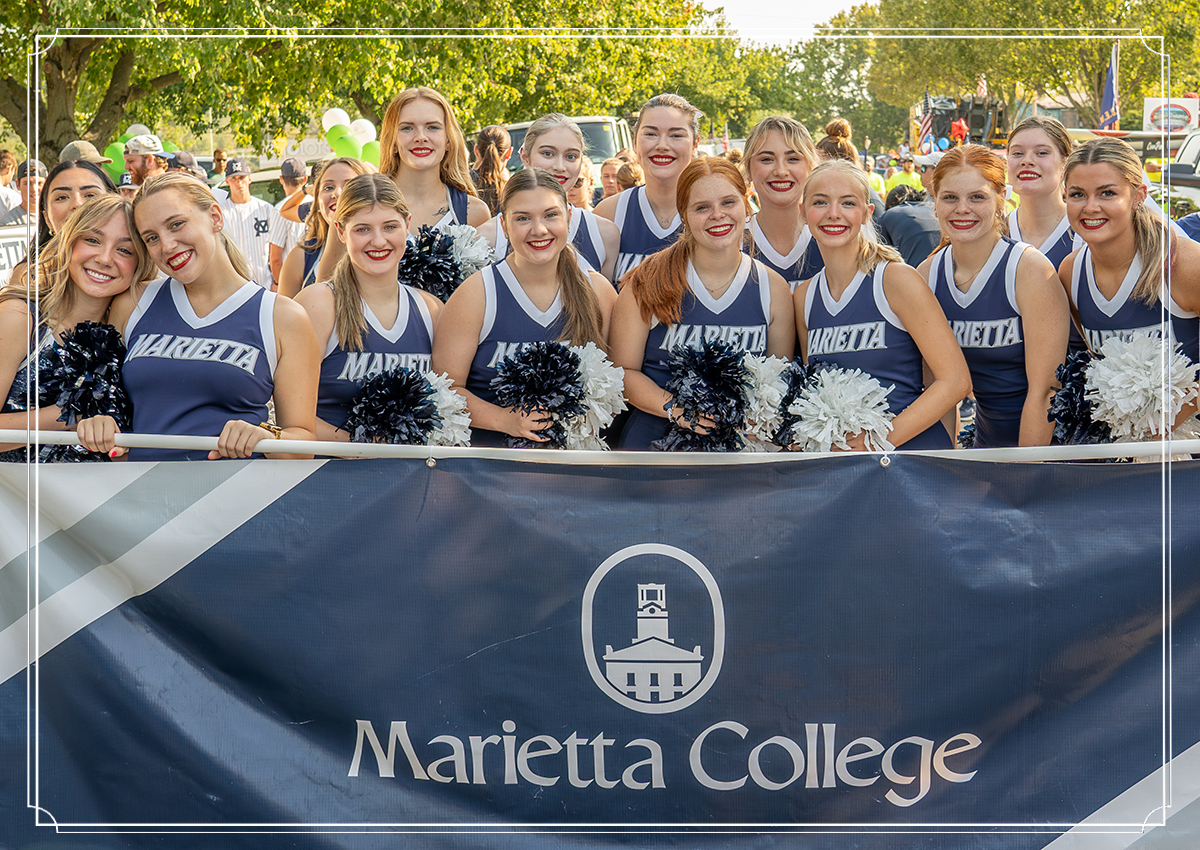 Cheerleaders hold a Marietta College banner and pom poms in community parade