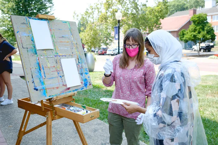 Faculty member Jolene Powell working with a student outside on an oil painting