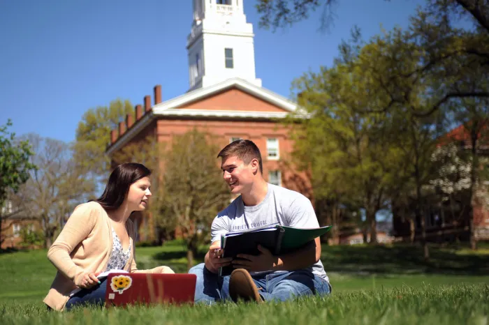 Female and male student sitting in the grass at DU Field