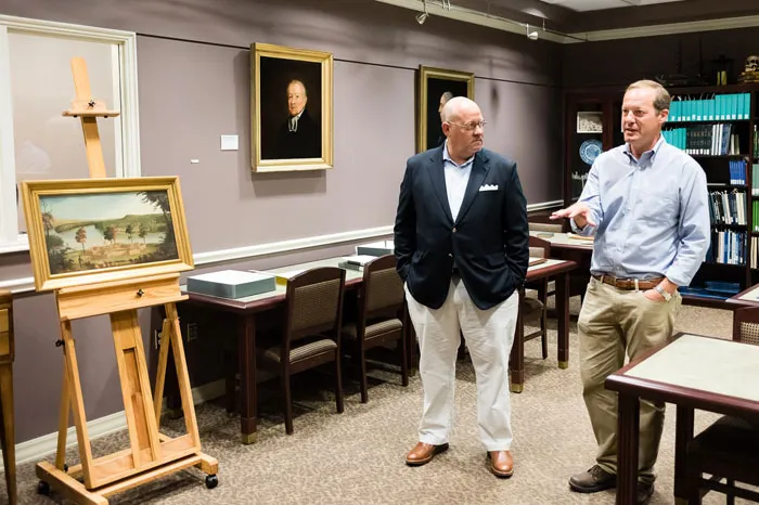 Two men in the library talking about an old painting